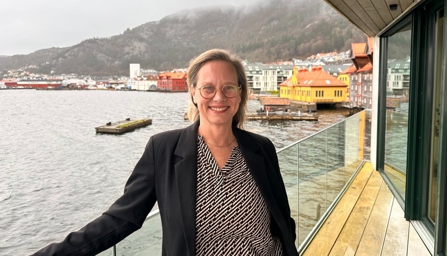 Solveig i svart dressjakke smiler på brygge foran hav