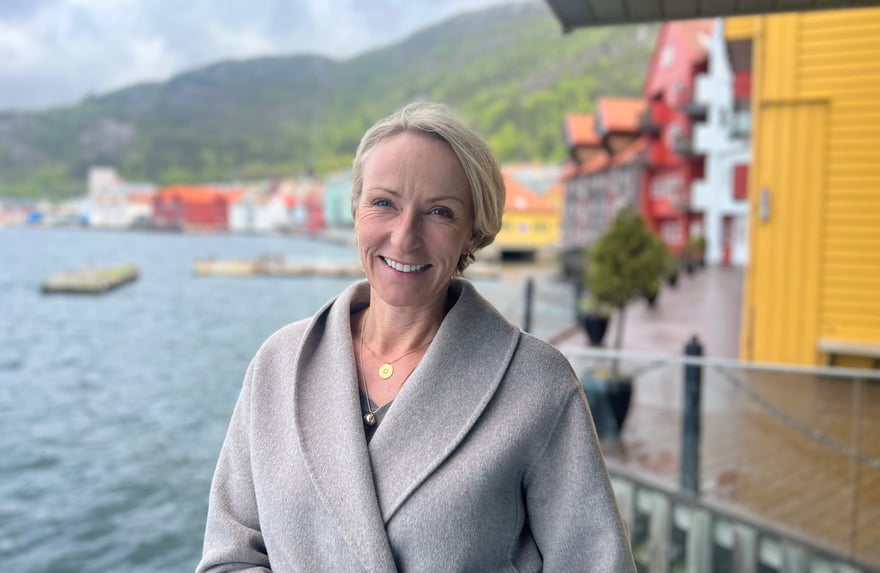 Stine smiler i beige kåpe foran havet