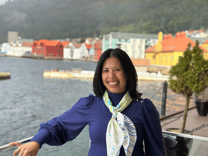 Maria i blå bluse foran hav og brygge