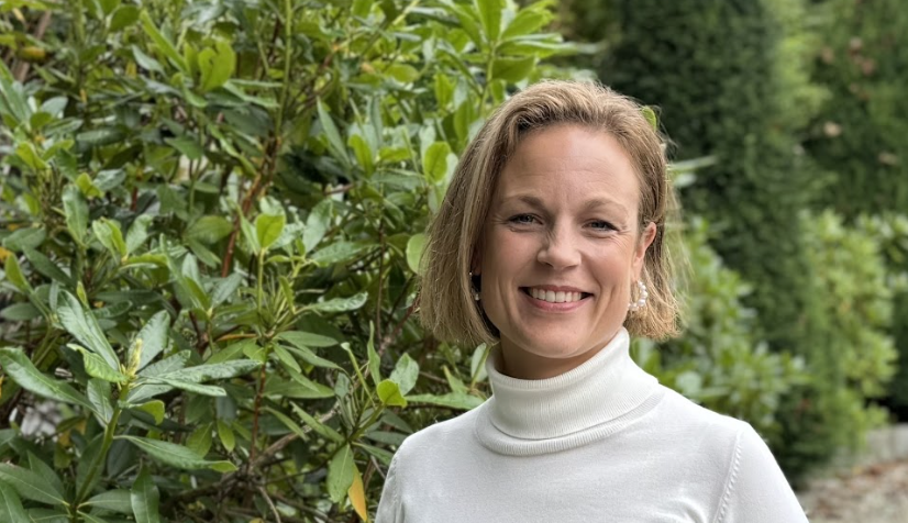 Kvinne (Tove) i hvit genser som smiler foran en stor grønn hekk