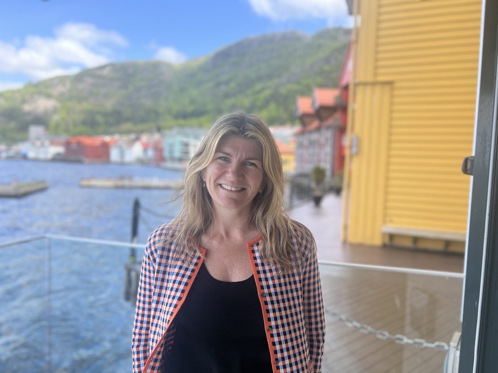 Vivian smiler foran blå himmel i fargerik jakke