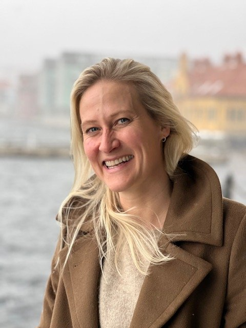 Stine som smiler i kåpe foran sjø